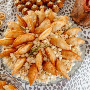 A variety of savory snacks including empanadas and popcorn on a leopard print tablecloth for a party setting.