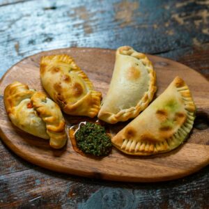 Appetizing baked empanadas served with chimichurri sauce on a wooden board. Perfect for food lovers.