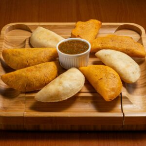Delicious assortment of crispy empanadas with a spicy dipping sauce on a wooden serving tray.