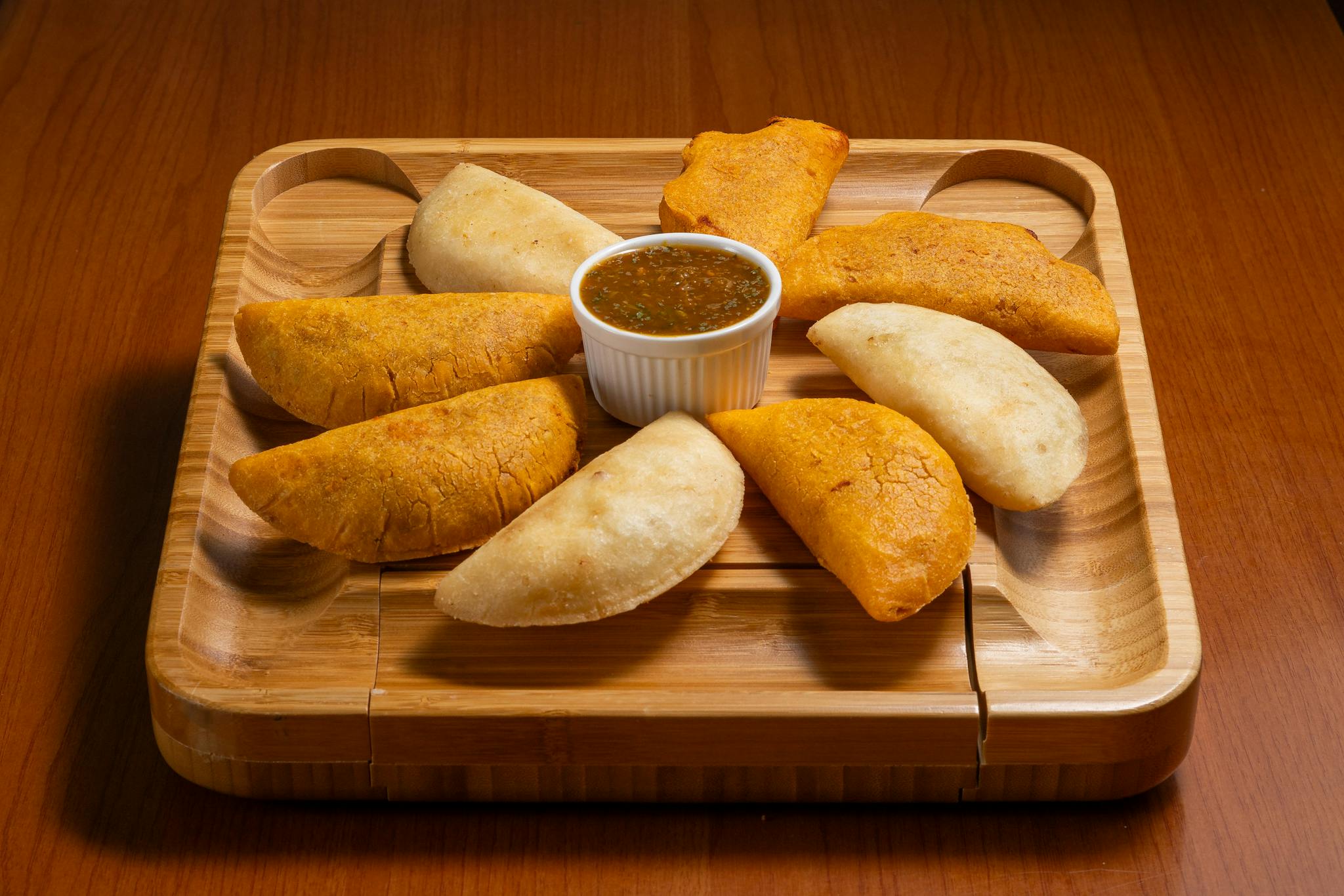 Delicious assortment of crispy empanadas with a spicy dipping sauce on a wooden serving tray.