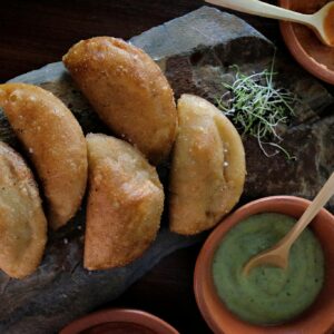 Golden empanadas served with various creamy dipping sauces on rustic stone.
